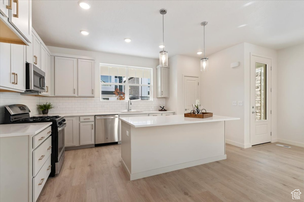 Kitchen with appliances with stainless steel finishes, a sink, light wood-style flooring, backsplash, and light countertops