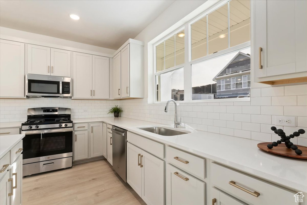 Kitchen featuring appliances with stainless steel finishes, a sink, decorative backsplash, light countertops, and light wood finished floors