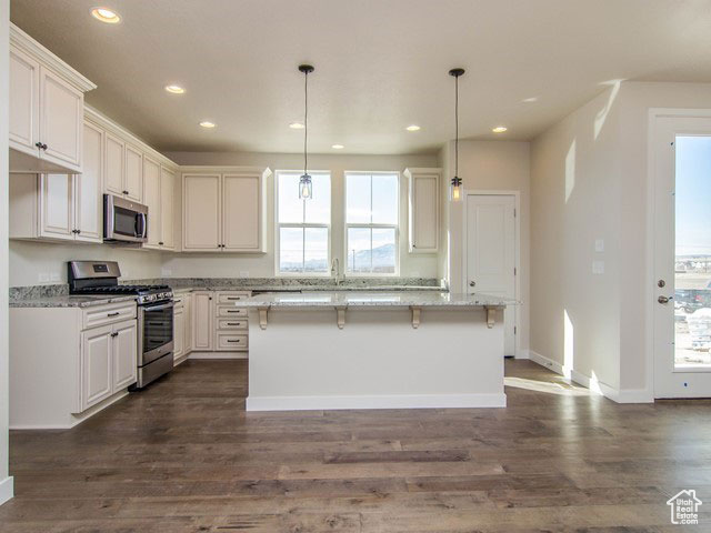 Kitchen with appliances with stainless steel finishes, recessed lighting, dark wood finished floors, baseboards, and light stone counters
