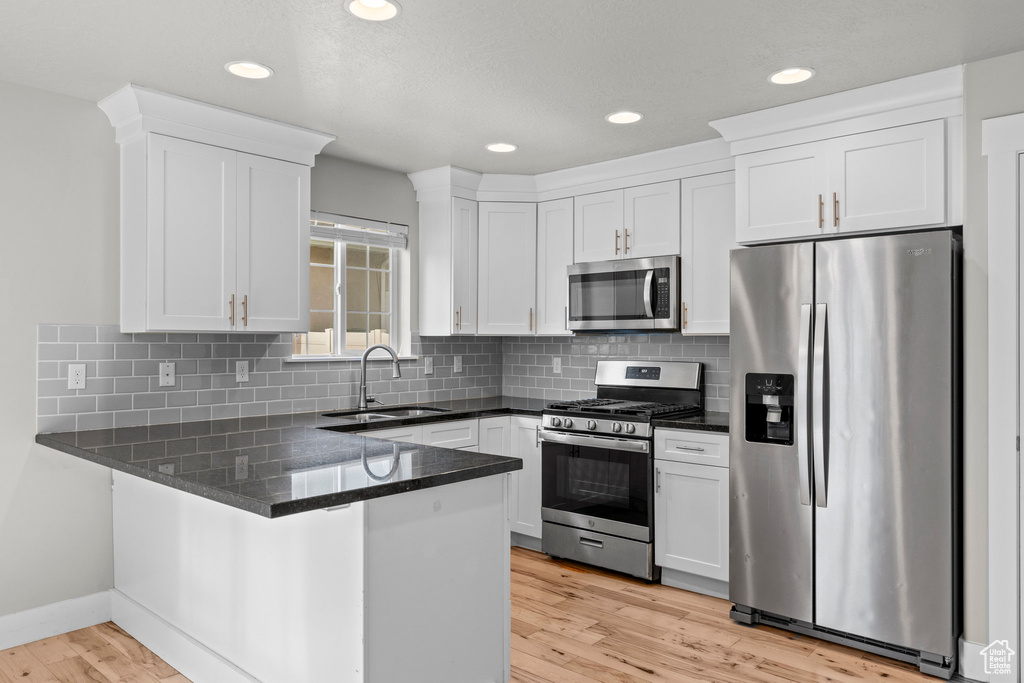 Kitchen featuring stainless steel appliances, a sink, a peninsula, white cabinetry, and light wood-style floors