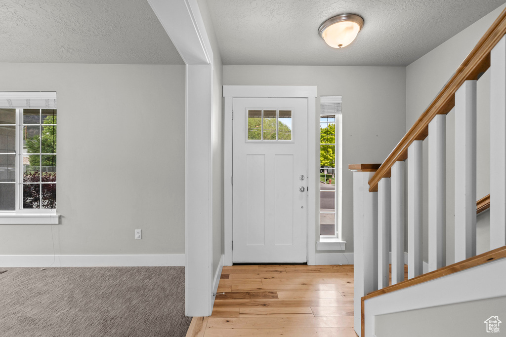 Foyer with a textured ceiling, stairs, plenty of natural light, light wood-type flooring, and baseboards