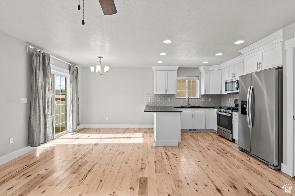 Kitchen featuring stainless steel appliances, a sink, dark countertops, white cabinets, and light wood-type flooring