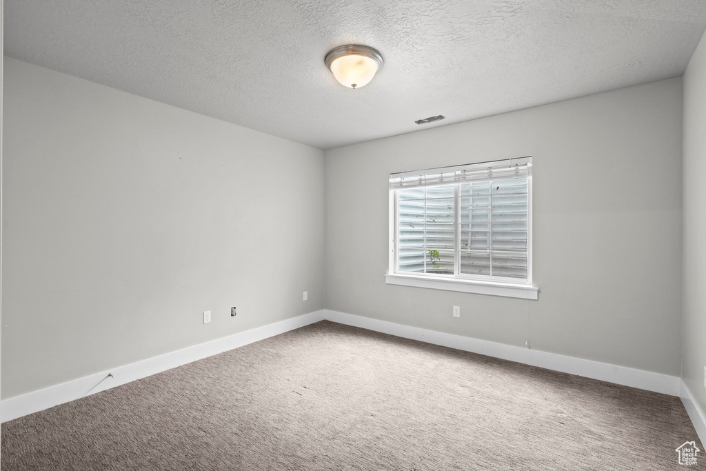 Empty room with carpet flooring, baseboards, and a textured ceiling