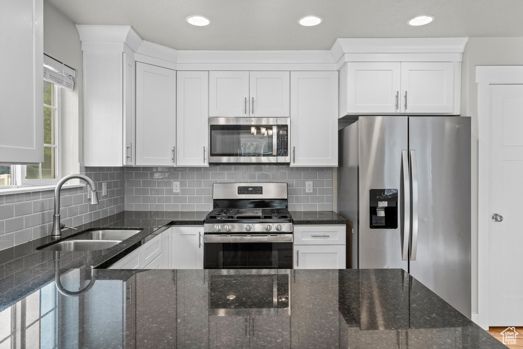 Kitchen featuring stainless steel appliances, a sink, white cabinets, dark stone counters, and recessed lighting