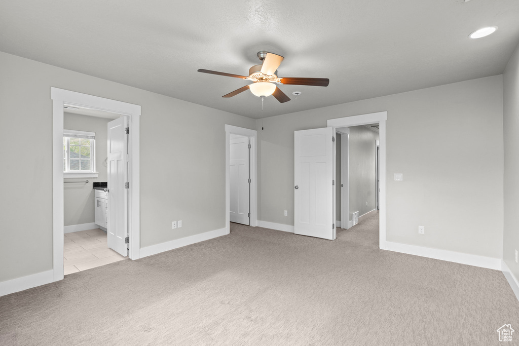 Unfurnished bedroom with light carpet, baseboards, ensuite bathroom, and ceiling fan
