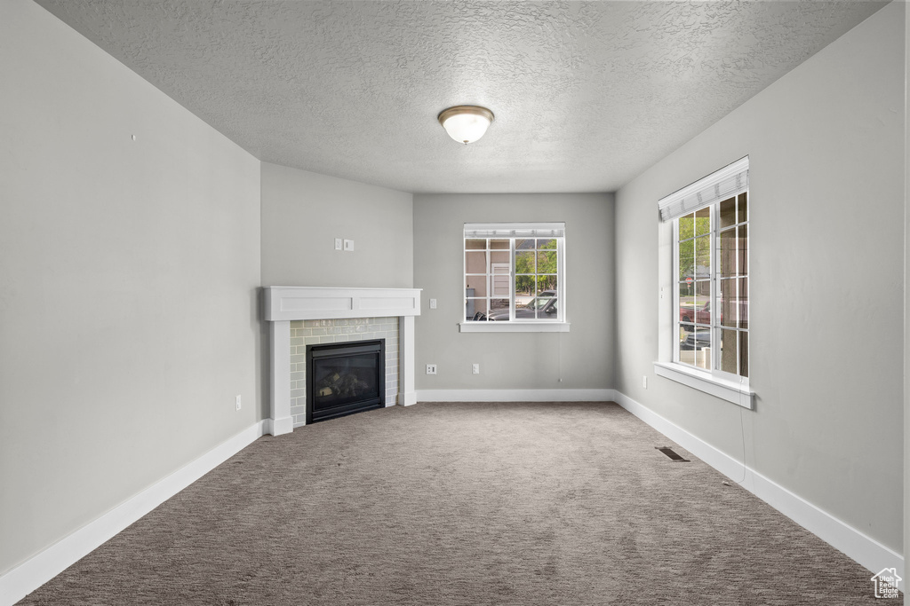 Unfurnished living room featuring a textured ceiling, carpet floors, a brick fireplace, and baseboards