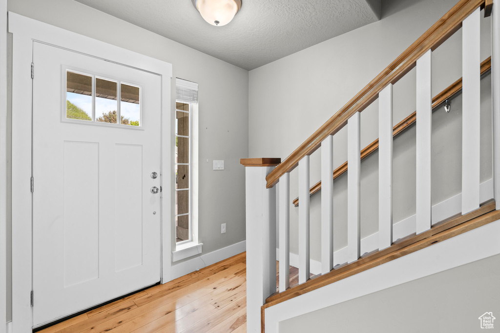 Entrance foyer with light wood-style flooring, a textured ceiling, and baseboards