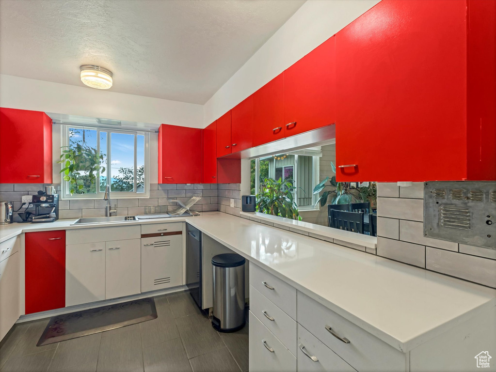Kitchen with a sink, red cabinets, backsplash, light countertops, and a textured ceiling