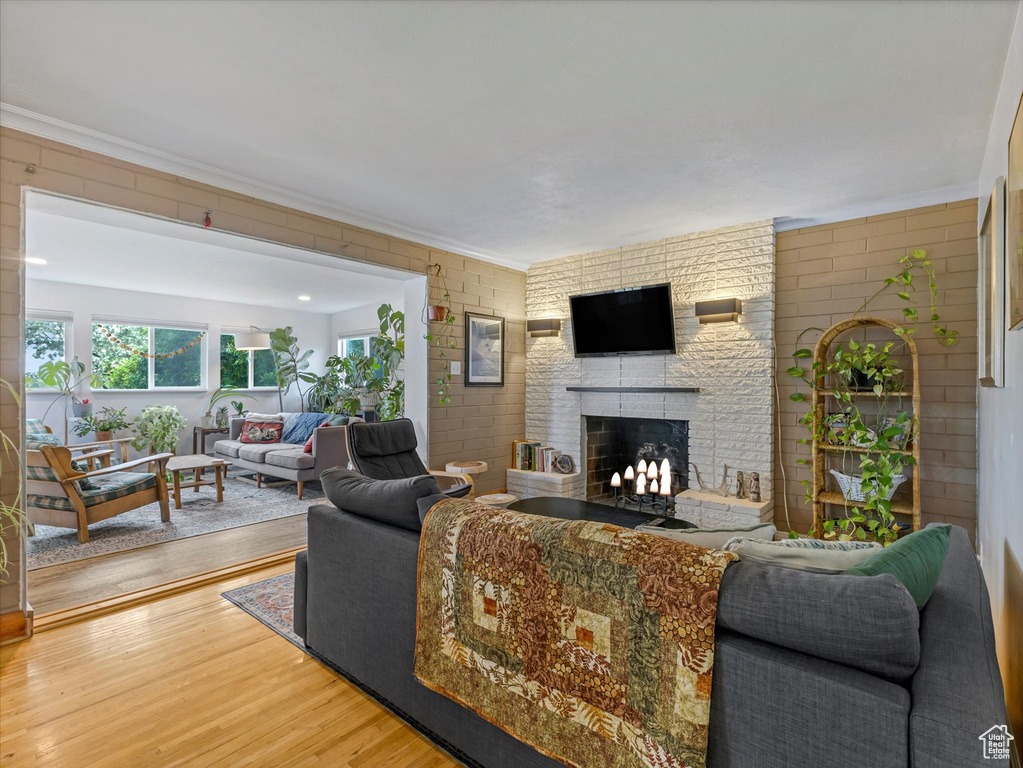Living area featuring a large fireplace, wood finished floors, crown molding, and brick wall