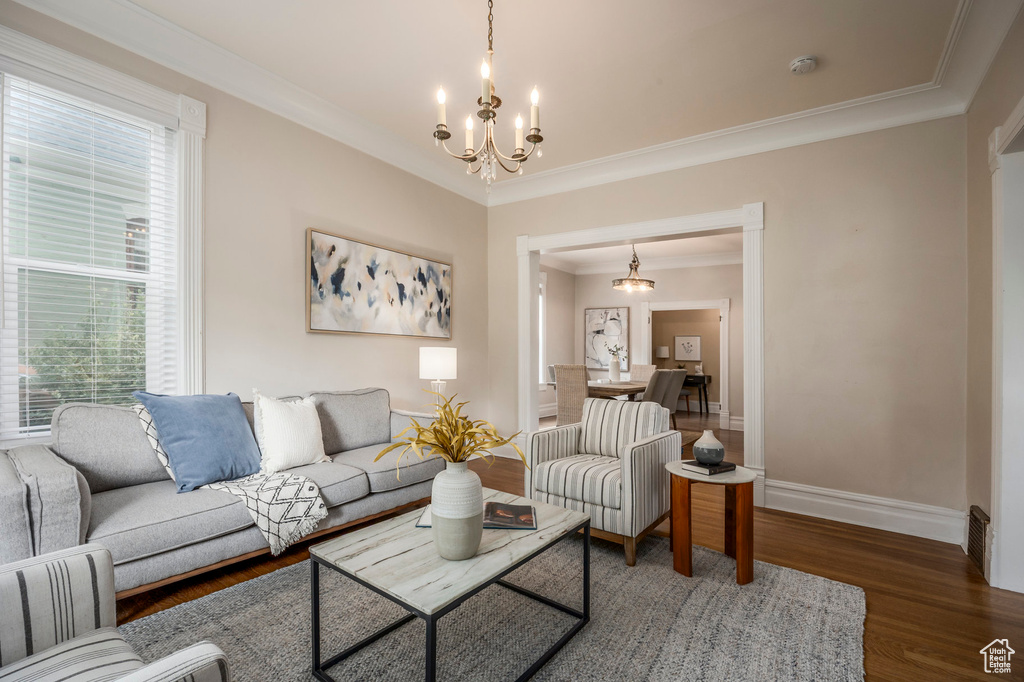 Living room with a chandelier, baseboards, crown molding, and wood finished floors
