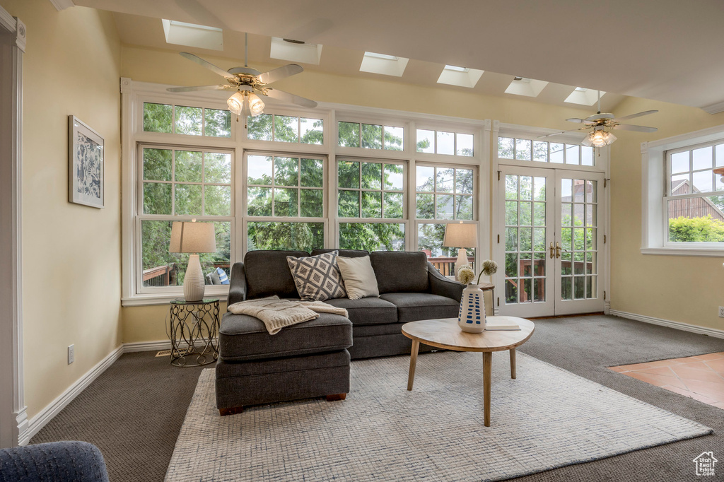 Carpeted living room with a ceiling fan, a skylight, baseboards, and french doors