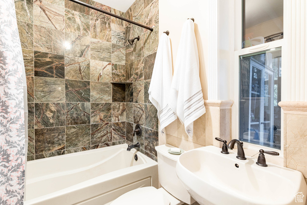 Full bathroom featuring a sink, shower / tub combination, tile walls, and toilet
