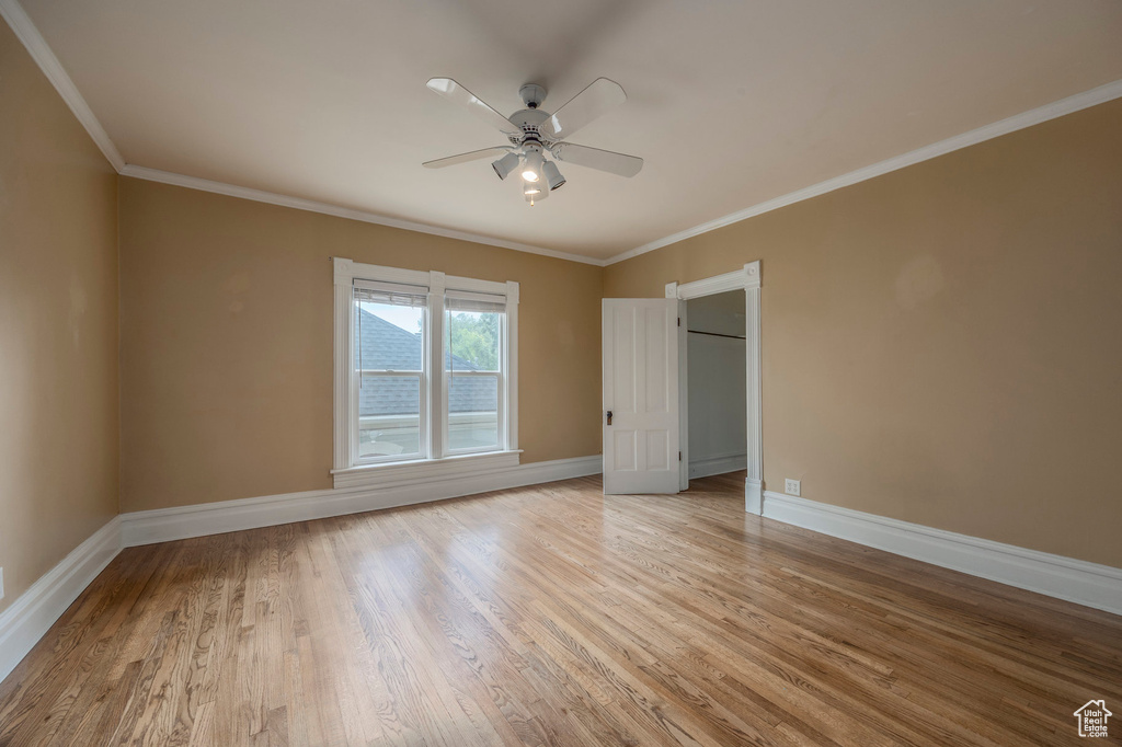 Unfurnished bedroom with light wood-style flooring, ornamental molding, baseboards, ceiling fan, and a walk in closet