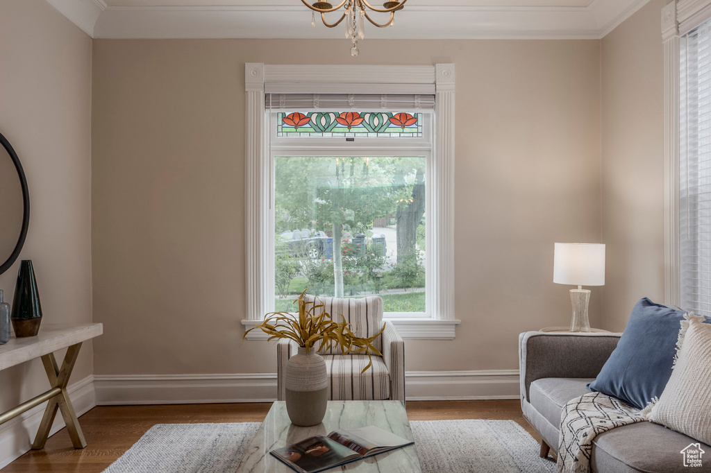 Living area with wood finished floors, baseboards, ornamental molding, and a chandelier