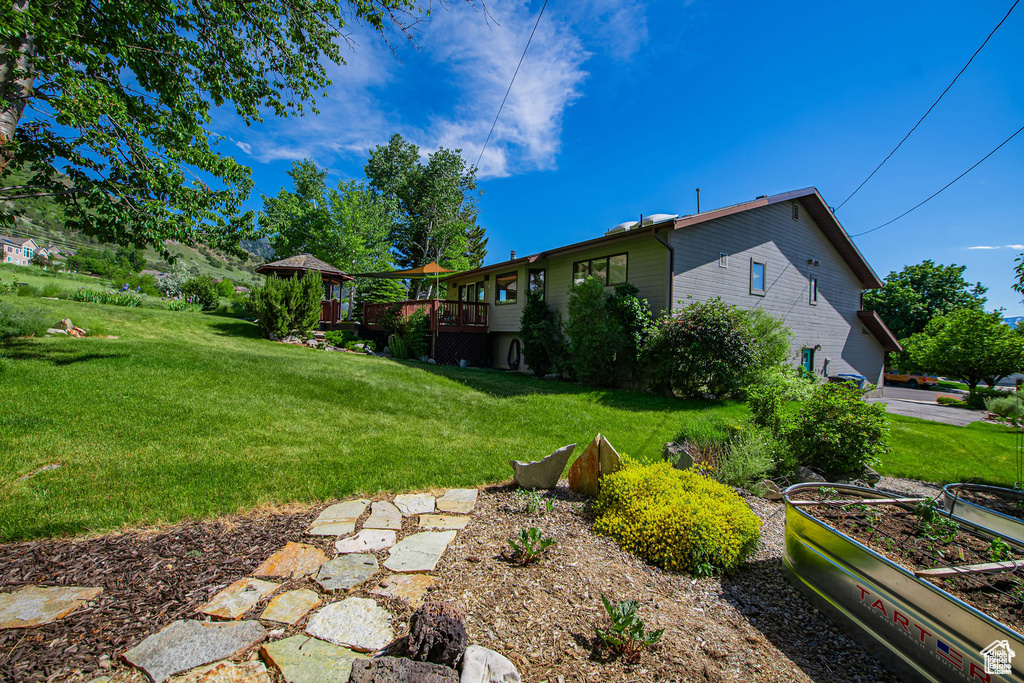 View of green lawn featuring a garden and a deck