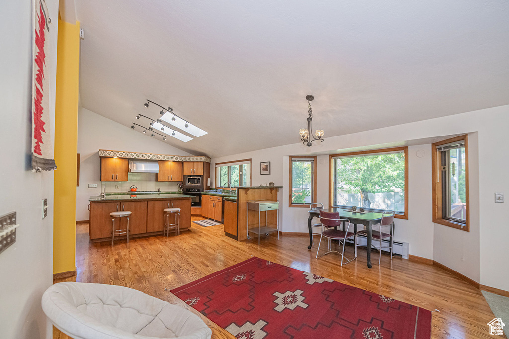 Kitchen with brown cabinetry, stainless steel microwave, dark countertops, wall chimney exhaust hood, and light wood-style floors