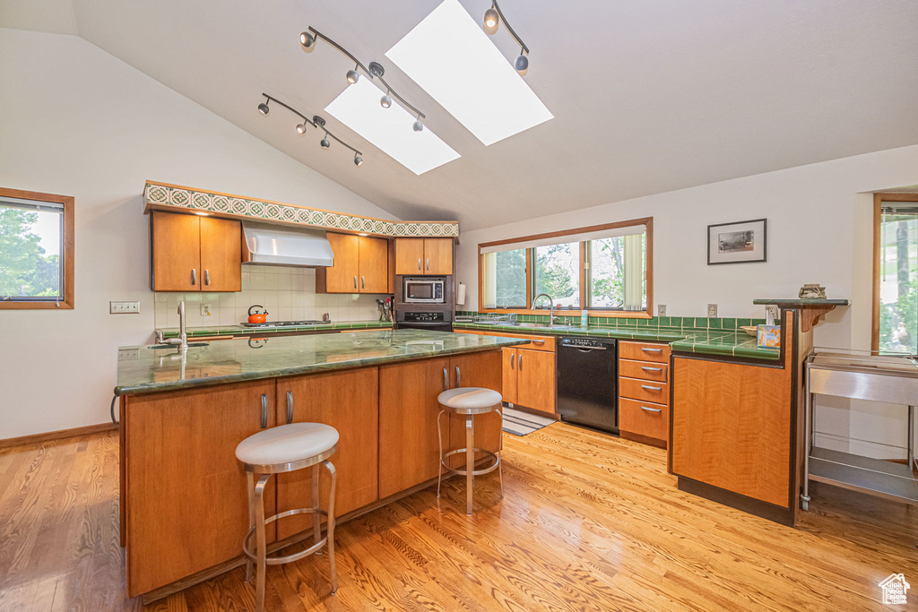 Kitchen with appliances with stainless steel finishes, a skylight, vaulted ceiling, wall chimney exhaust hood, and a sink