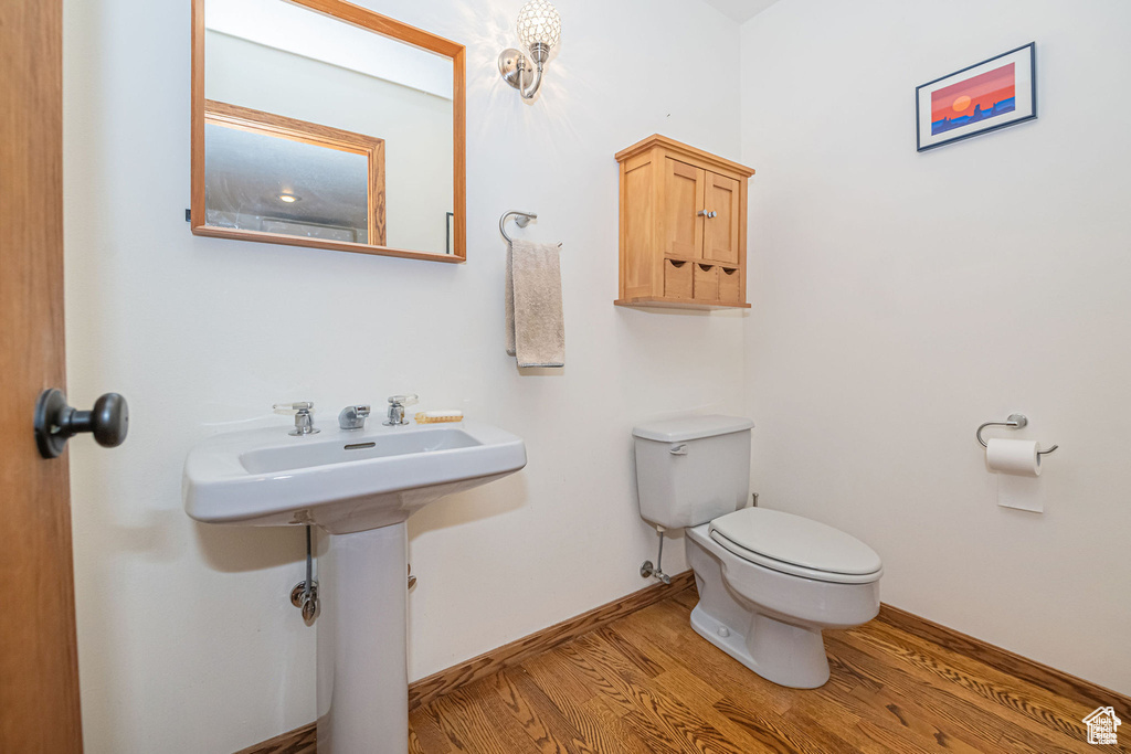 Half bathroom featuring wood finished floors, toilet, and baseboards
