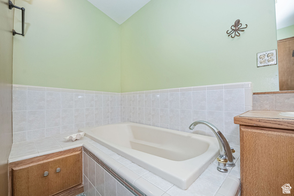 Full bathroom featuring a bath, vanity, tile walls, and vaulted ceiling