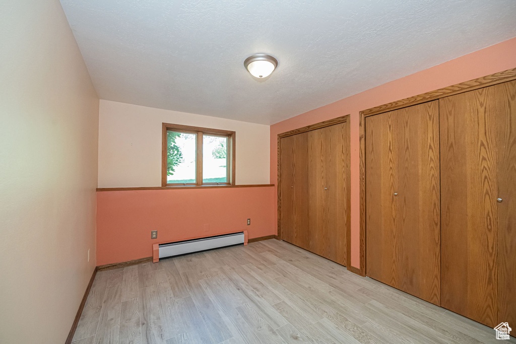 Unfurnished bedroom with a baseboard heating unit, light wood-style floors, multiple closets, and baseboards