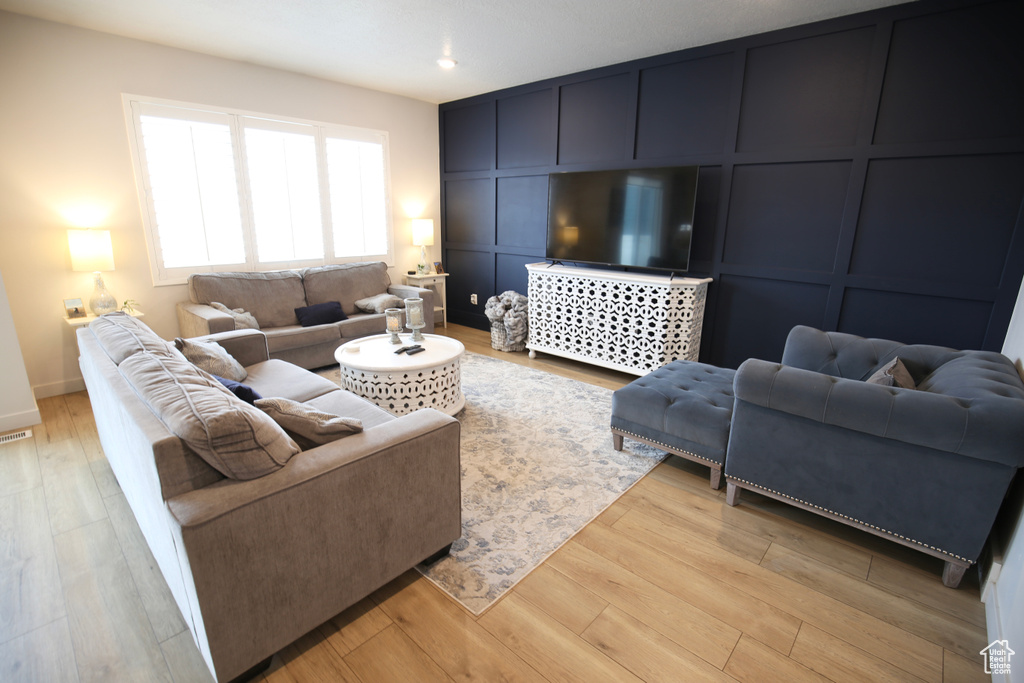 Living room featuring a decorative wall, light wood-type flooring, recessed lighting, and baseboards