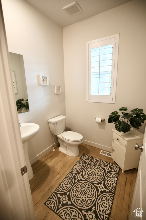 Half bath with toilet, wood finished floors, baseboards, and a sink