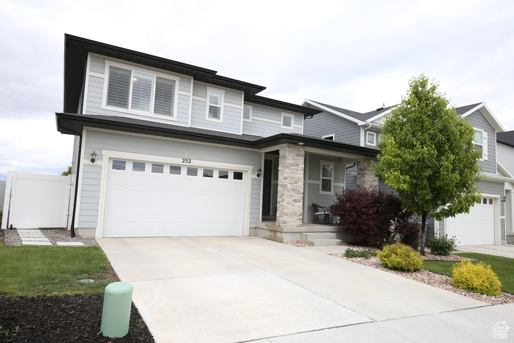 View of front of property with covered porch, a garage, concrete driveway, and fence