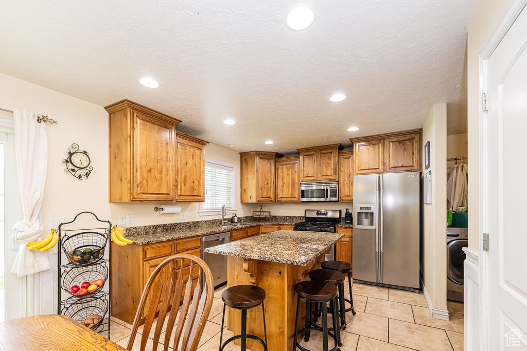 Kitchen featuring appliances with stainless steel finishes, brown cabinets, a breakfast bar area, a sink, and light tile patterned floors