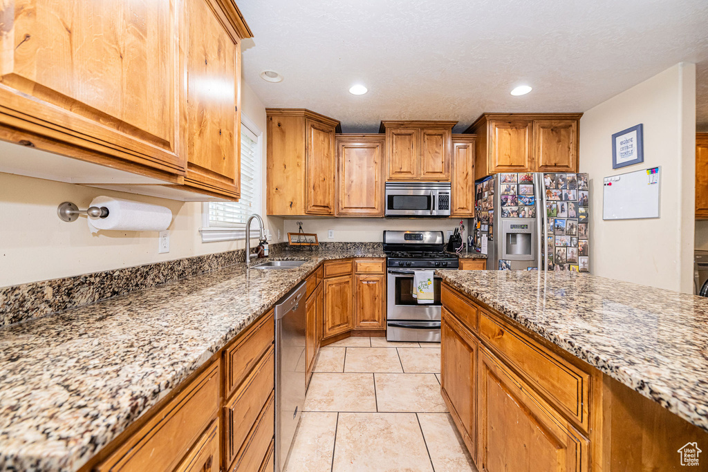 Kitchen featuring stainless steel appliances, a sink, light stone countertops, brown cabinets, and recessed lighting