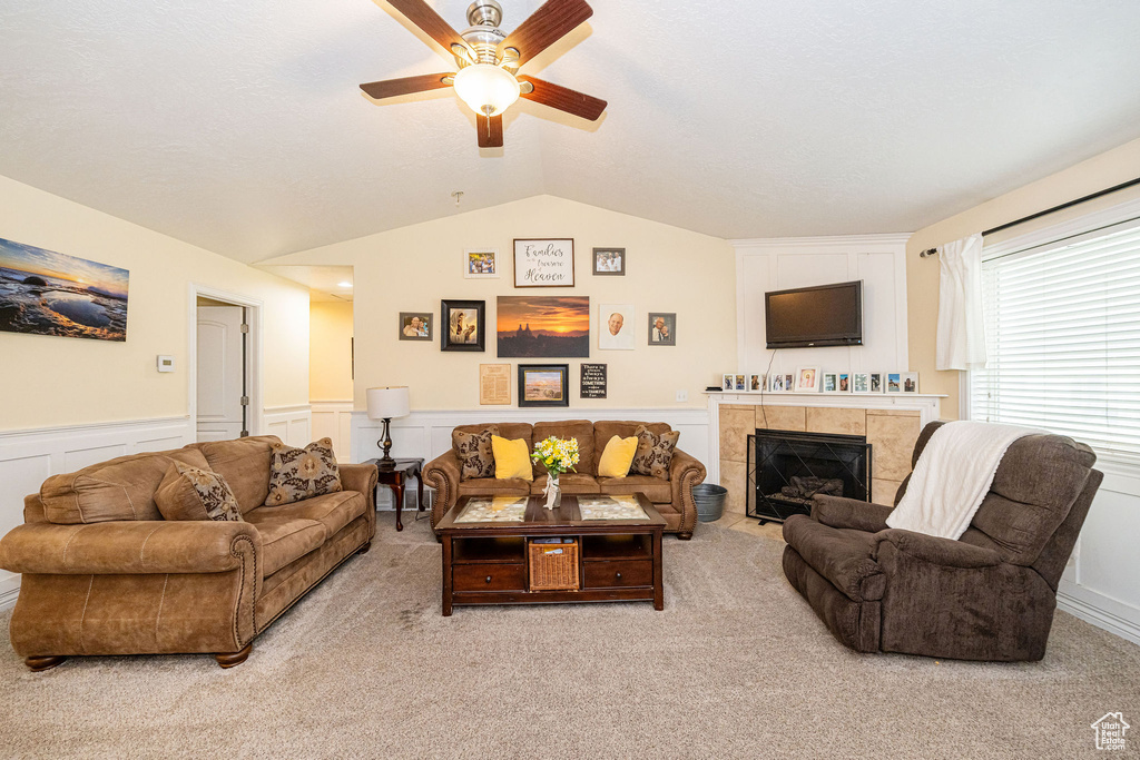Living area with vaulted ceiling, a ceiling fan, wainscoting, light colored carpet, and a tiled fireplace