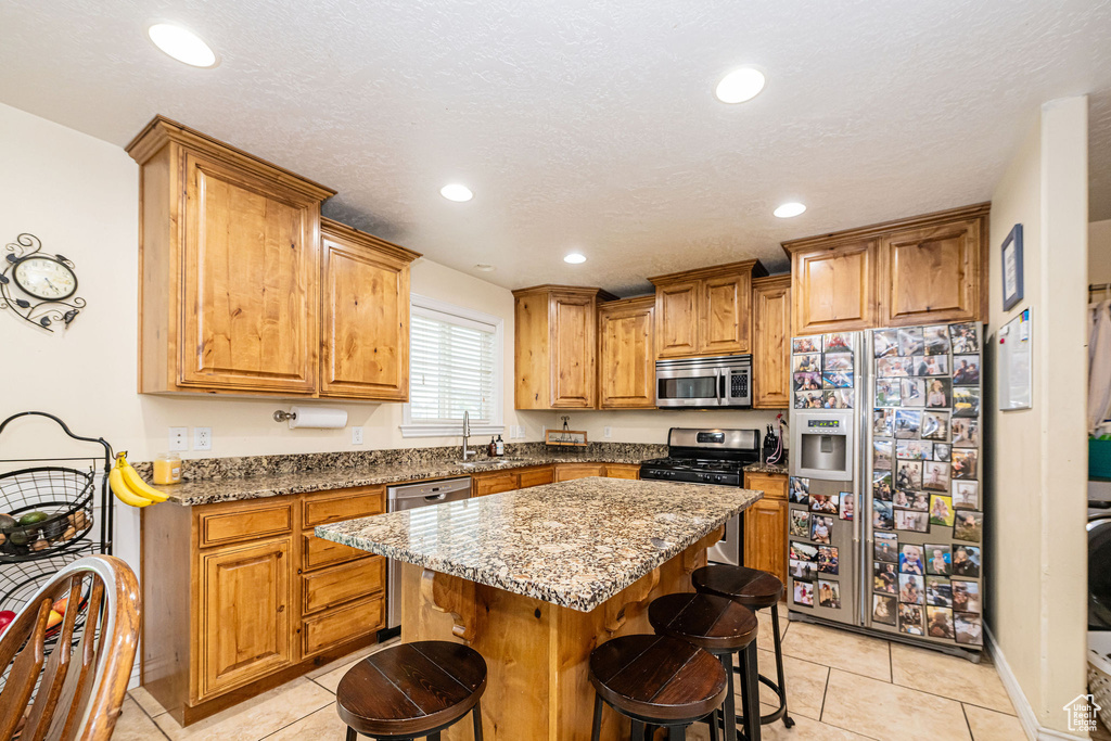 Kitchen with appliances with stainless steel finishes, a sink, light tile patterned floors, a kitchen bar, and recessed lighting