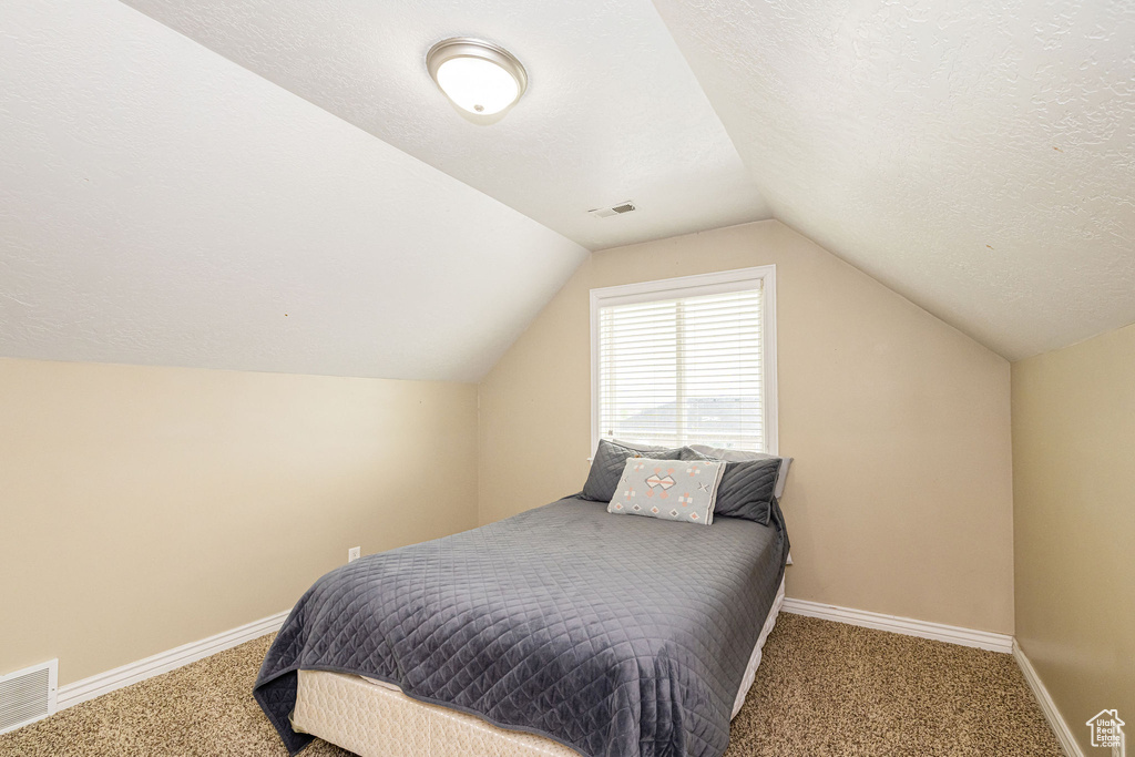 Bedroom with carpet, vaulted ceiling, baseboards, and a textured ceiling