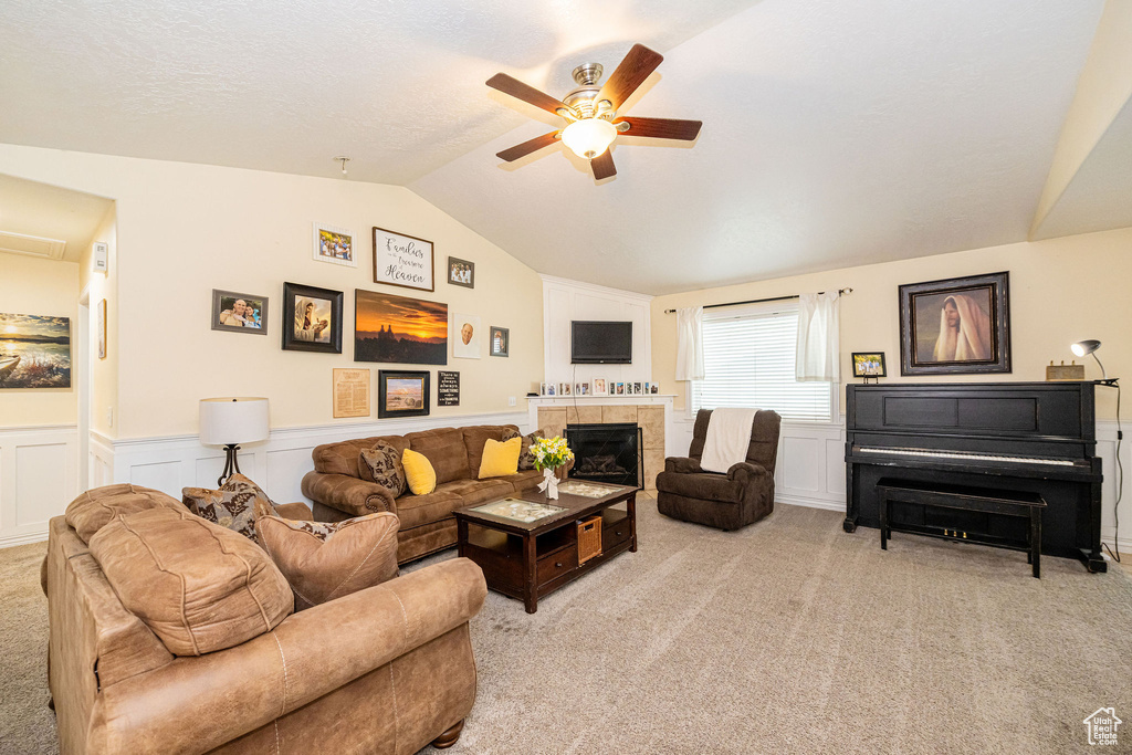 Living area featuring lofted ceiling, ceiling fan, light carpet, a wainscoted wall, and a tiled fireplace