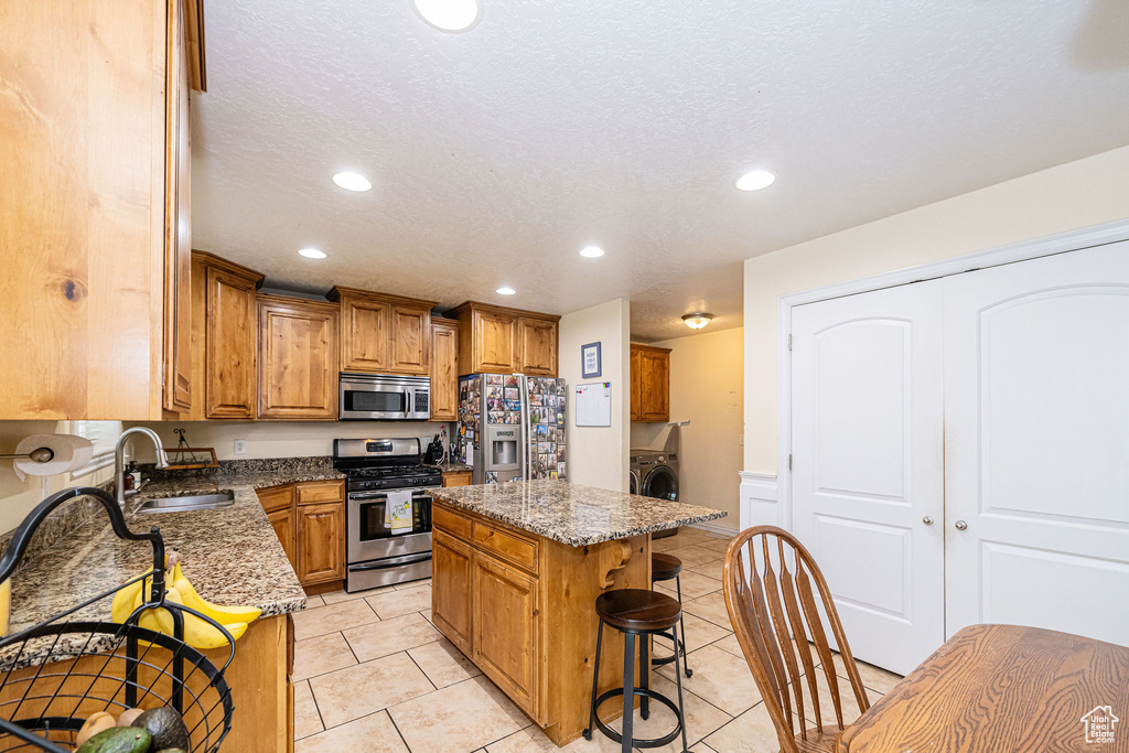 Kitchen with appliances with stainless steel finishes, a sink, stone countertops, a kitchen breakfast bar, and recessed lighting