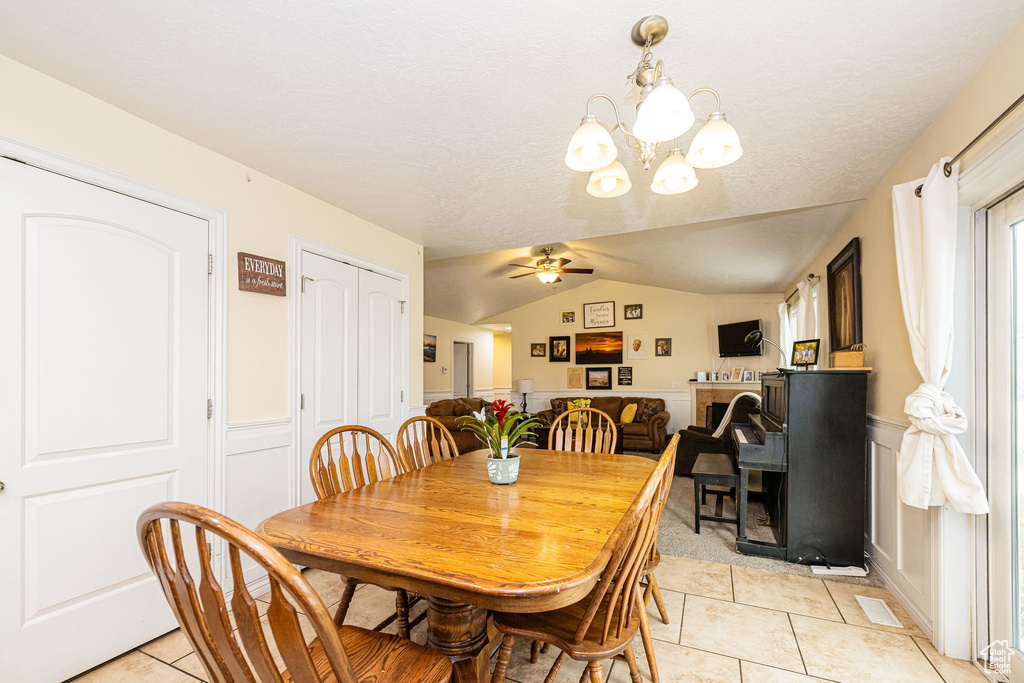 Dining area with light tile patterned floors, a ceiling fan, wainscoting, lofted ceiling, and a chandelier