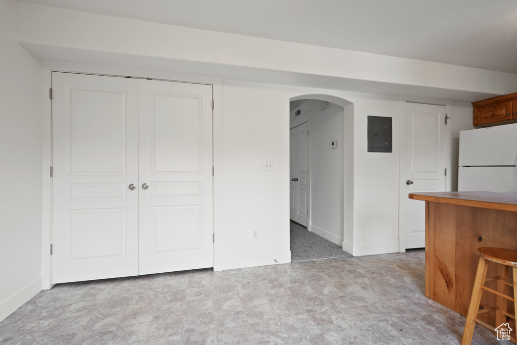 Interior space featuring freestanding refrigerator, electric panel, arched walkways, and baseboards