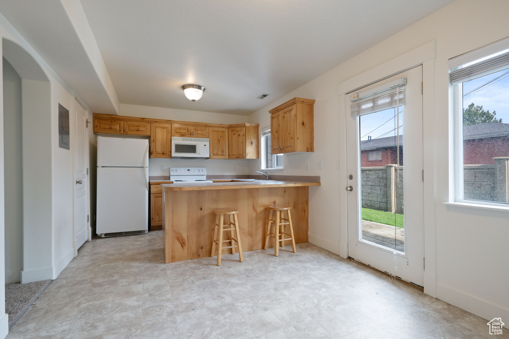 Kitchen with white appliances, healthy amount of natural light, a peninsula, and light countertops