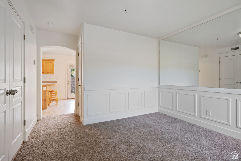 Carpeted empty room with arched walkways, wainscoting, and a decorative wall
