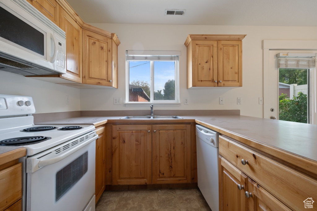 Kitchen featuring white appliances, a sink, light countertops, and light brown cabinetry