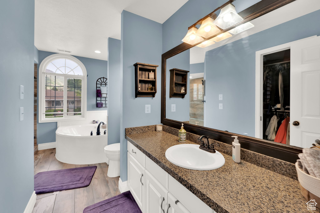 Bathroom featuring a soaking tub, wood finished floors, baseboards, vanity, and toilet