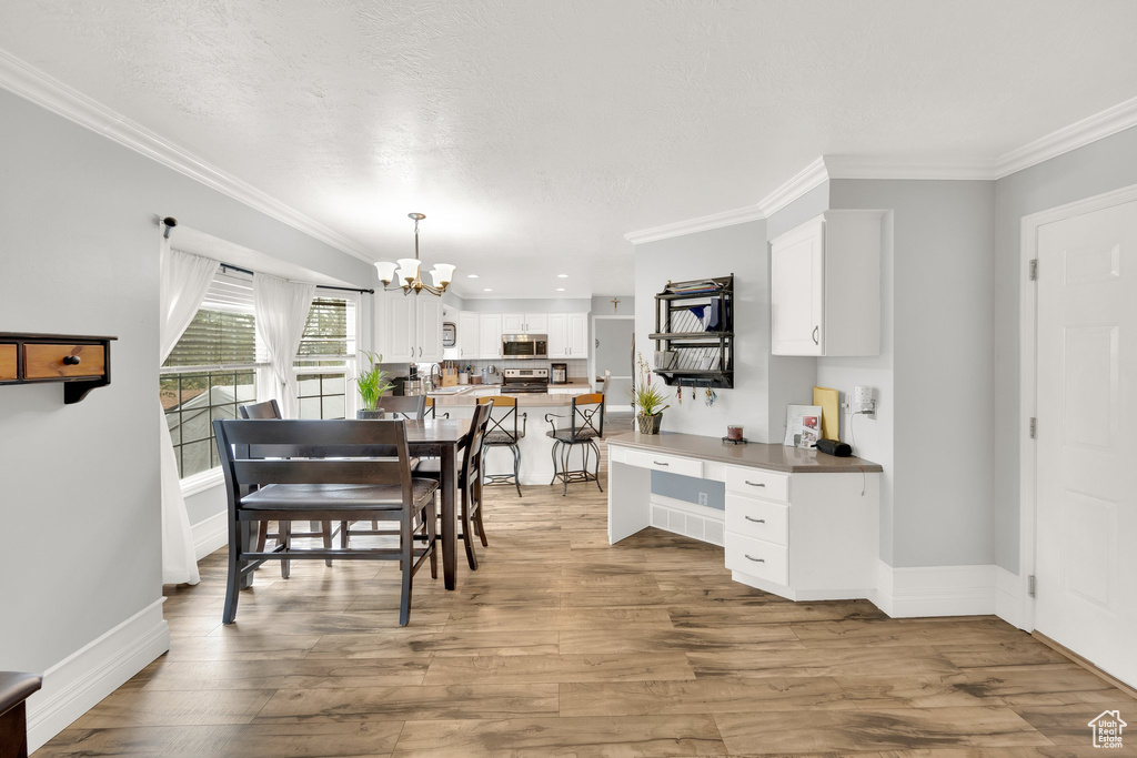 Dining room with a chandelier, crown molding, light wood-type flooring, baseboards, and a desk