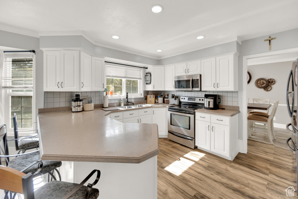 Kitchen with stainless steel appliances, a sink, a peninsula, a breakfast bar area, and crown molding