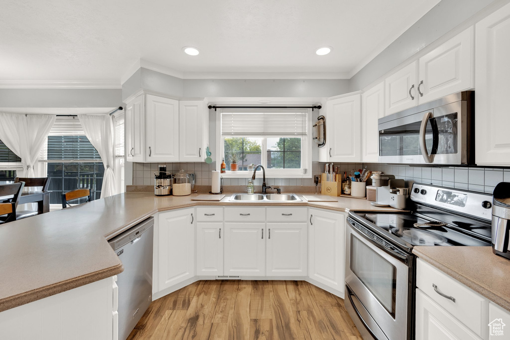 Kitchen featuring stainless steel appliances, a sink, light wood-style flooring, ornamental molding, and backsplash