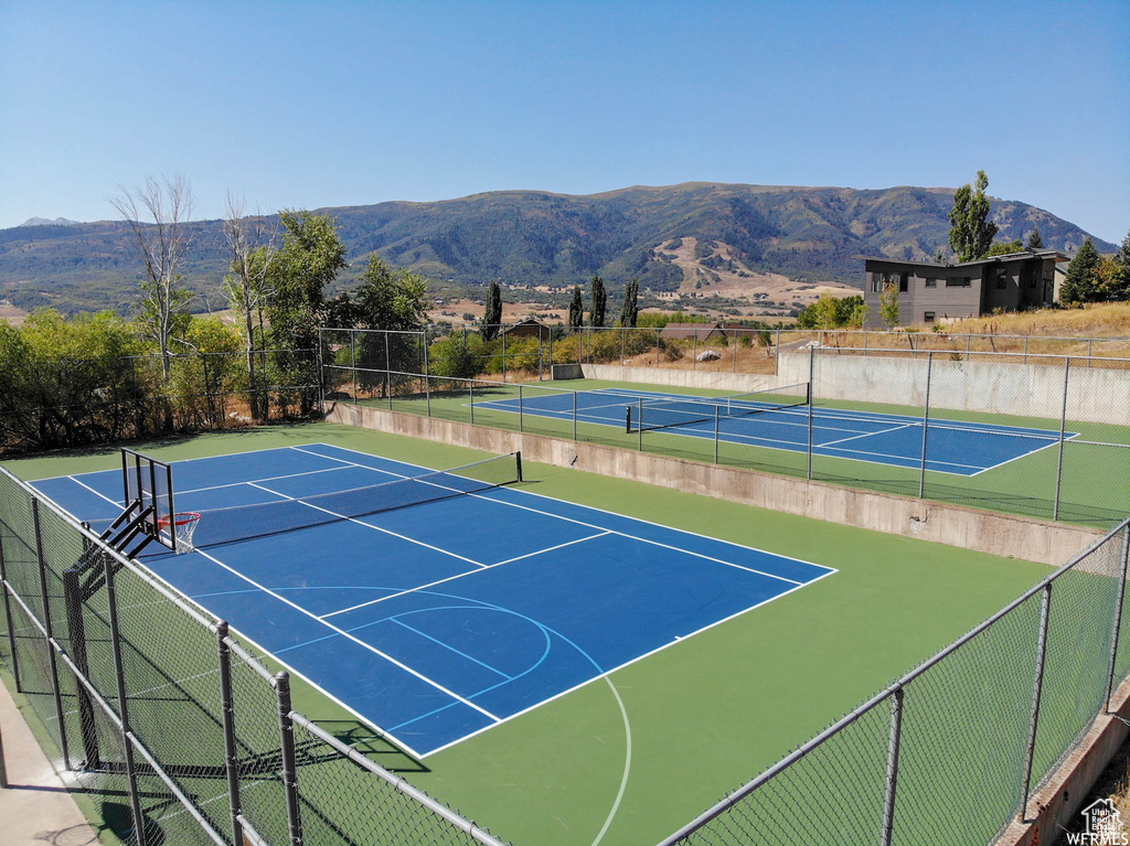View of tennis court with community basketball court, fence, and a mountain view