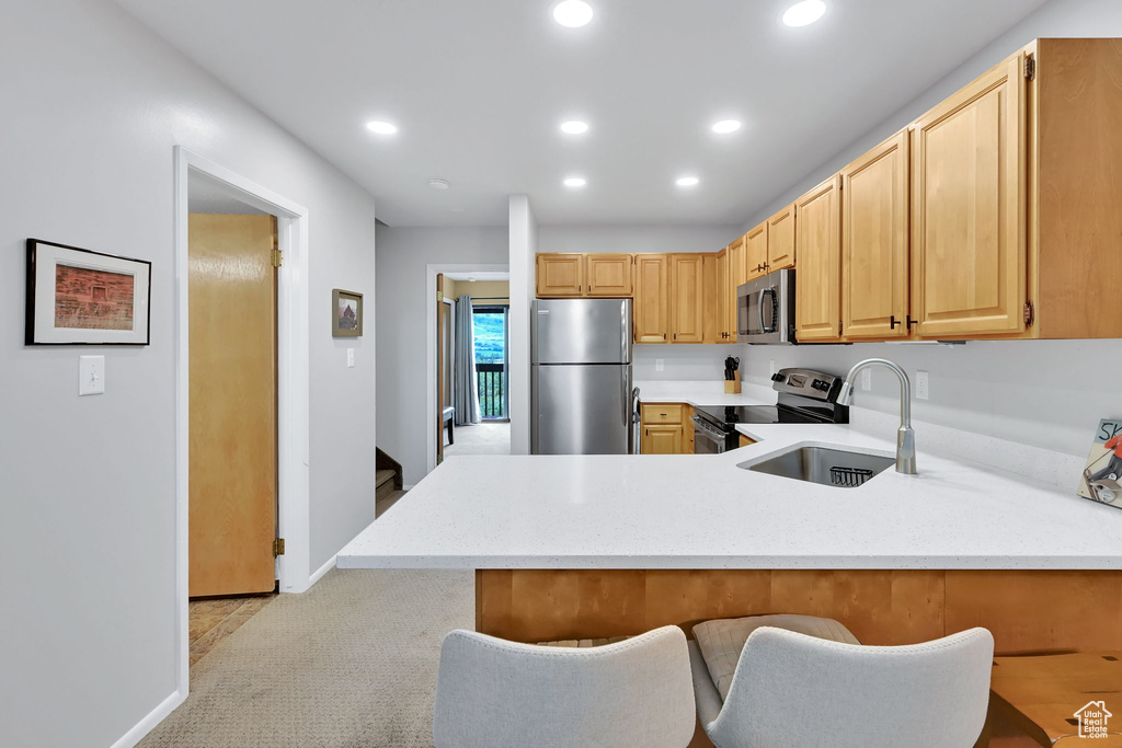 Kitchen featuring stainless steel appliances, a sink, a peninsula, recessed lighting, and light colored carpet