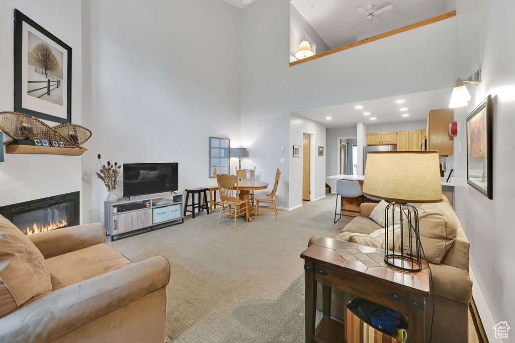 Living room featuring light colored carpet, a glass covered fireplace, a high ceiling, baseboards, and recessed lighting