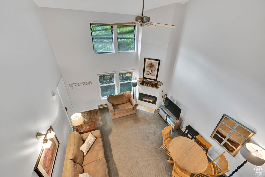 Living room with a high ceiling, a glass covered fireplace, and ceiling fan