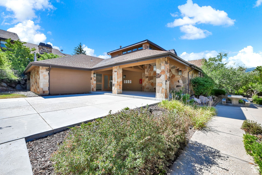 View of front of home featuring stone siding, concrete driveway, and a shingled roof
