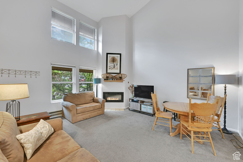 Living area featuring a high ceiling, a glass covered fireplace, carpet floors, a baseboard radiator, and baseboards