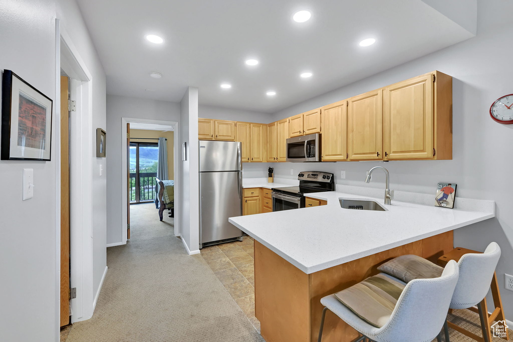 Kitchen featuring appliances with stainless steel finishes, a sink, light brown cabinetry, light countertops, and a peninsula